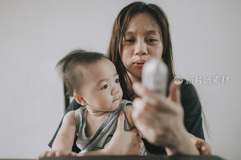 telemedicine asian  chinese mother checking her baby boy son body temperature using thermometer while consulting her pediatrician doctor online using laptop